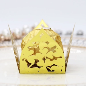 Detail of laser-cut gold candy box with clover patterns on a white porcelain plate