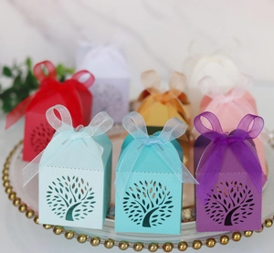 Laser-cut Tree of Life wedding favor boxes with colorful ribbon bows on a glass tray