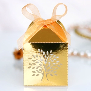 Close-up of golden laser-cut tree candy box with orange ribbon and metallic texture