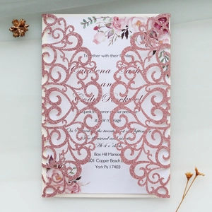 Close-up of laser-cut wedding invitation with rose gold glitter and floral inner card