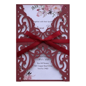 Macro shot of laser-cut burgundy invitation with floral insert and silk ribbon bow