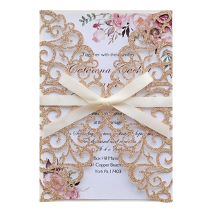 Close-up of laser-cut gold glitter wedding invitation with floral insert and cream ribbon bow
