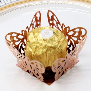 Detail of rose gold laser-cut butterfly candy box with intricate hollow design on a white plate