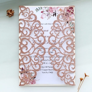 Detail of laser-cut rose gold glitter wedding invitation with floral insert and floral accents