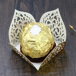 Detail of laser-cut hollow floral paper wrapper holding a chocolate on dark wood