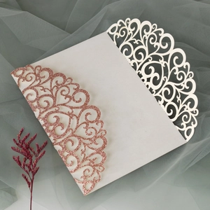Detail of laser cut scrollwork on rose gold glitter and ivory wedding invitation cover