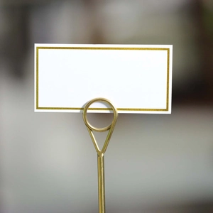 White place card with gold border on a gold metal stand for wedding table settings
