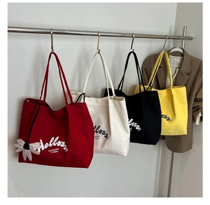 Row of canvas tote bags in red, white, black and yellow with flower pendants on a rack