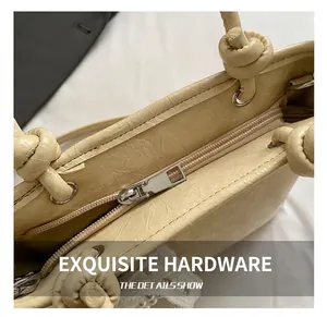 Detail of beige textured handbag showing smooth metal zipper and knotted handle craft