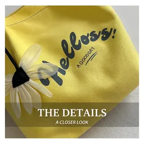Detail shot of yellow canvas tote bag featuring floral pendant and black artistic font print
