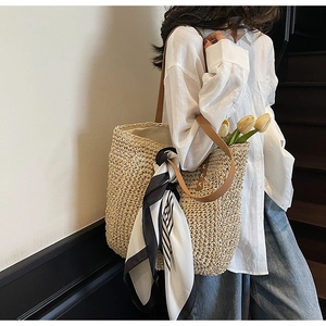 Detail of straw tote bag with brown leather handles and a striped silk scarf accent