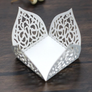 Top view of white laser-cut paper favor box with elegant floral patterns on wood texture