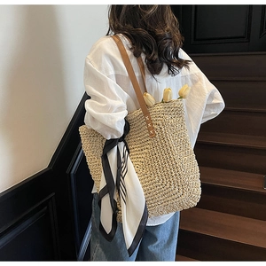 Detail of handwoven straw tote with leather straps and striped scarf on model