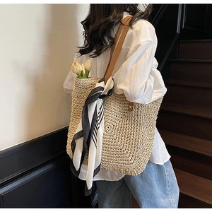 Close-up of woven straw tote bag with brown leather handles and striped scarf detail