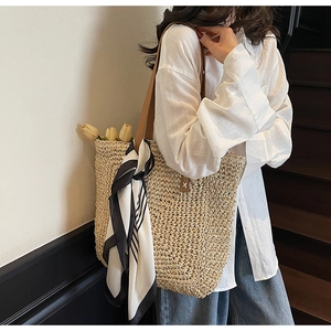 Detail of hand-woven straw tote with brown leather handles and striped silk scarf decoration