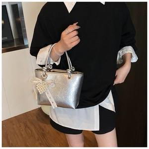Detail of silver metallic handbag featuring knot handles and pearl heart charm accessory