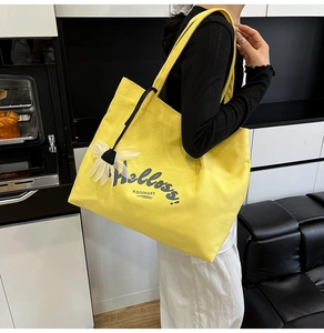 Detail of bright yellow canvas tote bag with Helloss print and white flower charm