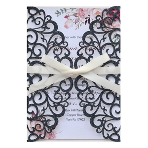 Detail of laser-cut black glitter wedding invitation with white ribbon and floral insert