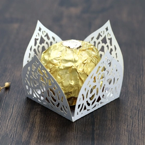 Detail of white laser-cut hollow lace candy box on dark wood with gold chocolate