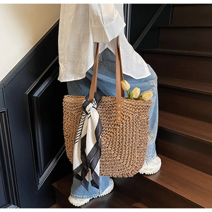 Detail of straw woven tote bag with brown leather straps and striped silk scarf decoration