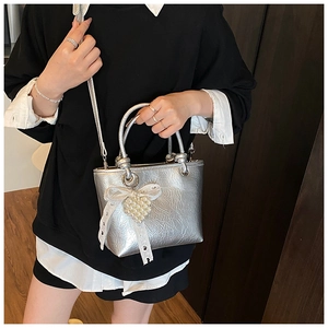 Detail of silver metallic bucket bag featuring lace bow and pearl heart charm accessory
