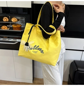 Detail of yellow canvas tote bag with Helloss print and white flower charm accessory