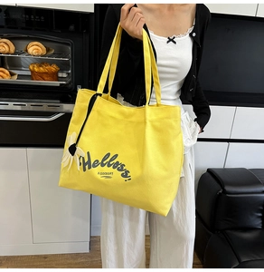 Detail of yellow canvas tote bag featuring black lettering and a white daisy pendant charm