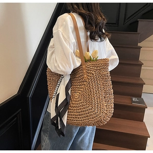 Detail of hand-woven straw tote bag with brown leather straps and geometric silk scarf