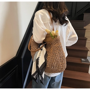 Detailed close-up of large straw tote bag with leather strap and decorative silk scarf