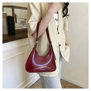 Detail of dark red underarm bag with glossy leather texture and FASHION & BAGS lettering