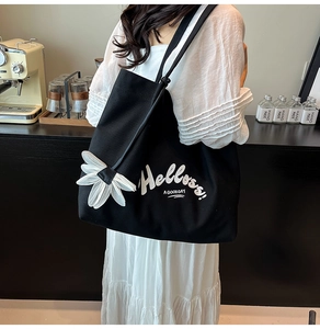 Detail of black canvas tote bag with white floral pendant and Hello print in a cafe setting