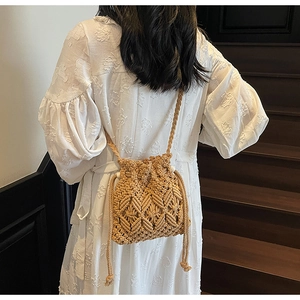 Detail of hand-woven straw bucket bag with drawstring tassels on a model