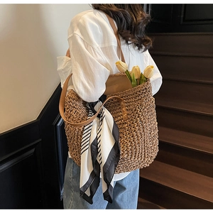 Detail of hand-woven straw tote with brown leather strap and decorative striped scarf