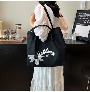 Detail of a large black canvas tote bag with Helloss print and white floral charm