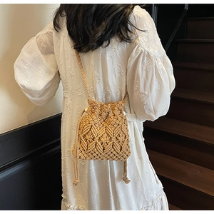 Woven straw drawstring bucket bag showing mesh texture on a model wearing white dress