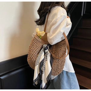 Detail of large woven straw tote bag with black and white striped scarf on brown strap