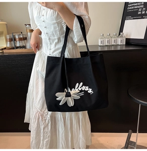 Close-up of black canvas tote bag with white art lettering and flower charm accessory