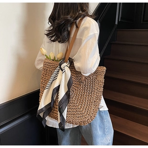 Detail of handwoven straw tote bag with brown leather handles and striped silk scarf