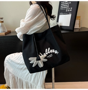 Detail of black canvas tote bag with white 'Helloss!' print and daisy charm on shoulder