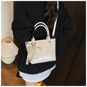 Detail of cream glossy patent leather bucket bag with lace bow and pearl heart charm