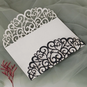 Detail of laser-cut glitter wedding invitation featuring intricate floral patterns and vine texture
