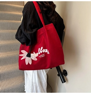 Close-up of red canvas tote bag with white lettering and a 3D floral charm