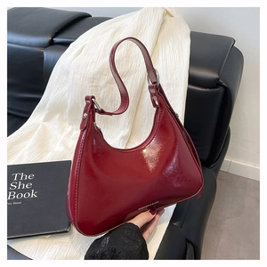 Detail of dark red crescent baguette bag showing glossy finish and silver metal ring