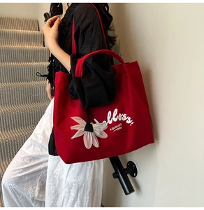 Close-up of red canvas tote bag featuring white 3D flower charm and Hello print