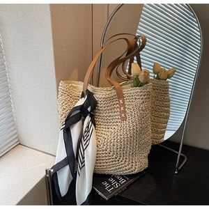 Detail of woven tote bag featuring brown leather handles and geometric silk scarf accent