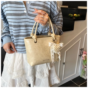 Detail of beige tote bag featuring knotted handles and pearl heart lace bow pendant