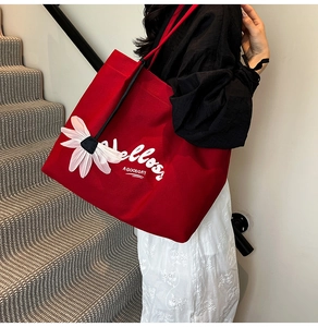 Detail of red canvas tote bag with 3D daisy flower and Hello typography on shoulder