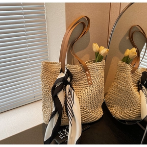 Detail view of woven straw tote bag with brown leather handles and striped silk scarf