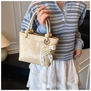 Close-up of cream-colored bucket bag with pearl heart charm and lace bow details