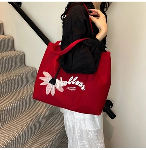 Detail of red canvas tote bag featuring white 3D daisy charm and artistic typography